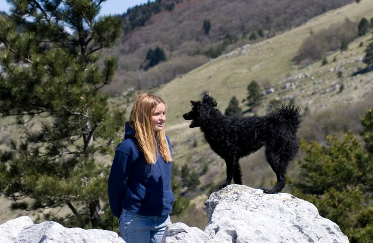 Jeune femme parlant à un chien noir devant des montagnes, symbolisant la communication animale.