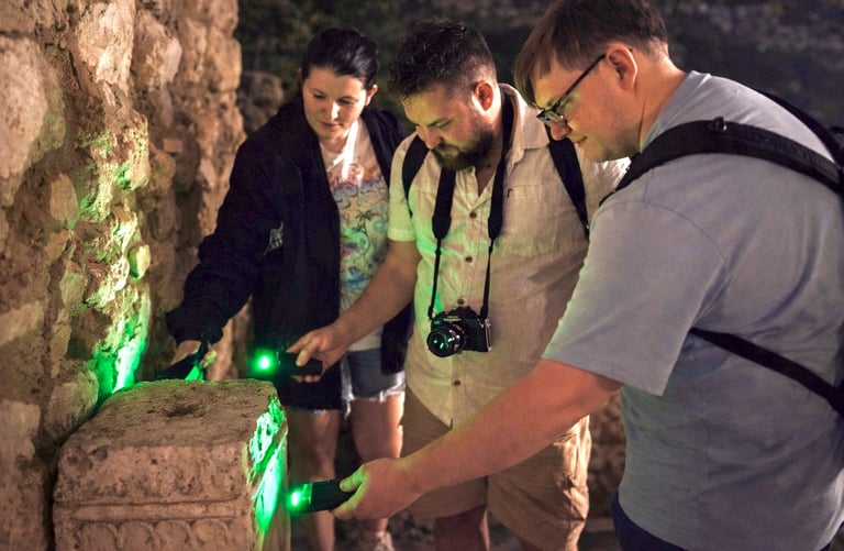 Tour participants examining ancient stone ruins with green UV lights during Athens Ghost Tour