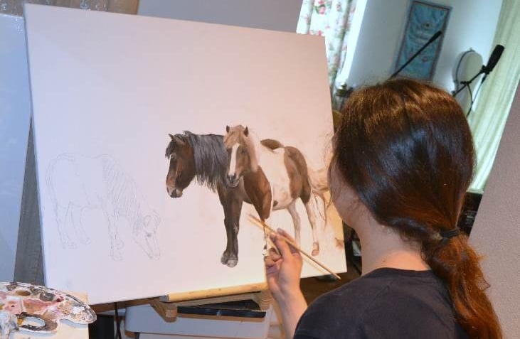 a woman is painting two ponies on a easel
