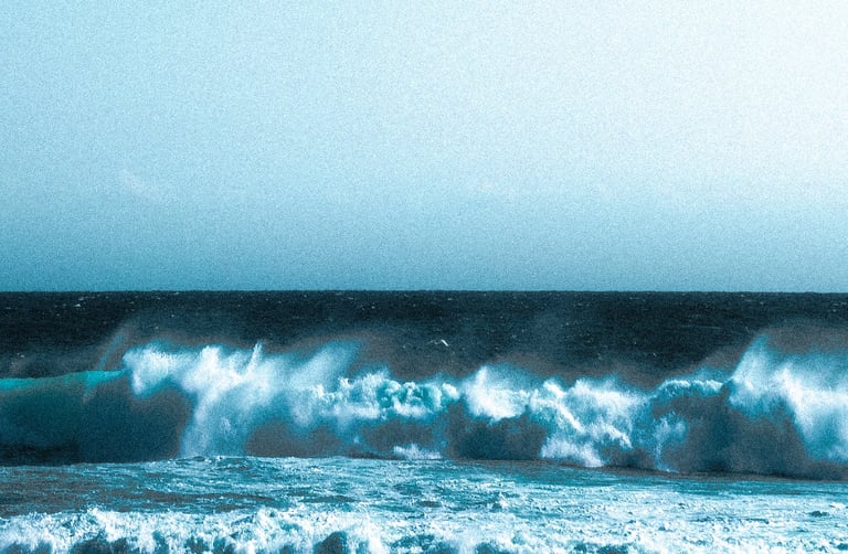 Dramatic blue ocean waves crashing onto a sandy beach under a clear sky.