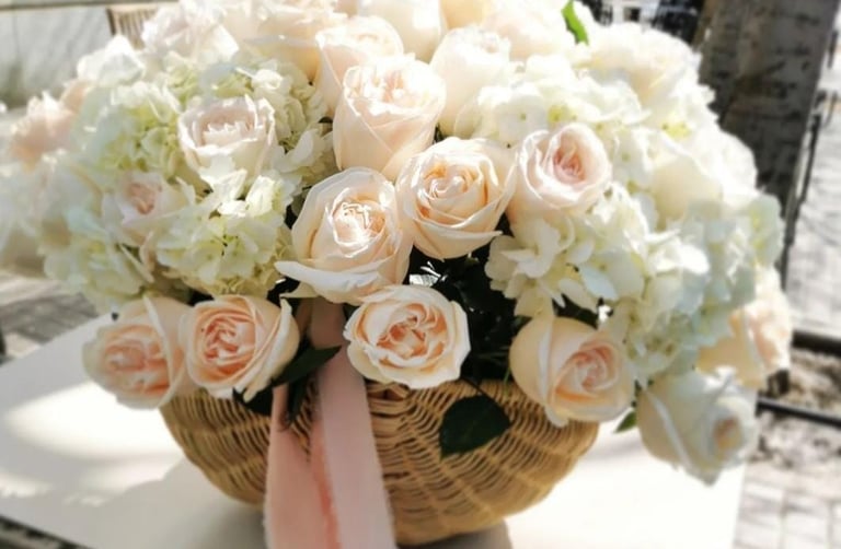 Elegant floral arrangement of peach roses and white hydrangeas in a wicker basket.
