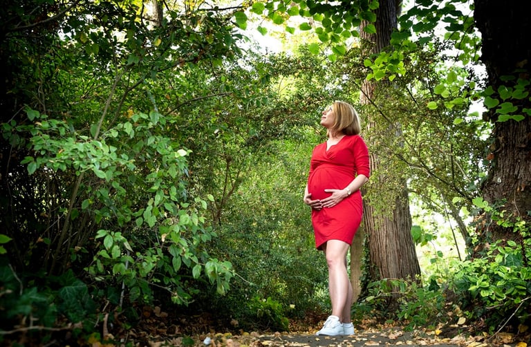 Photo d'une femme enceinte vêtue d'une robe rouge, debout dans une zone boisée