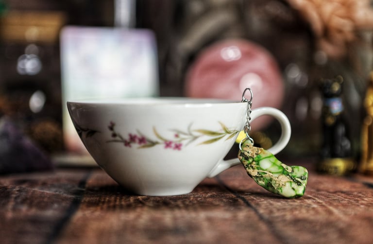 A tea cup with a green stone charm hanging from it