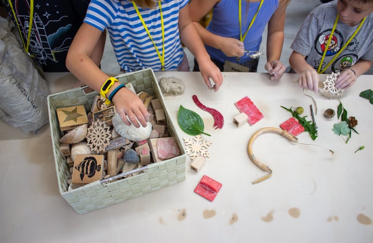 Children's hands reaching into a bin of stamps and supplies.
