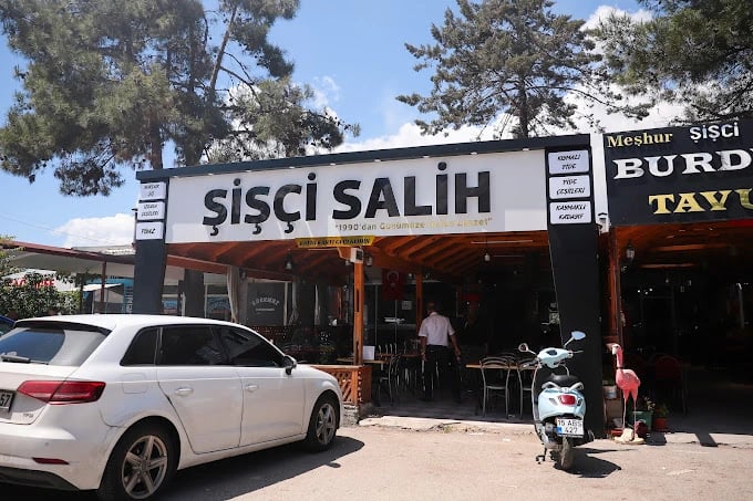 Sisci Salih restaurant storefront in Turkey with outdoor seating, a white car, and a blue scooter.
