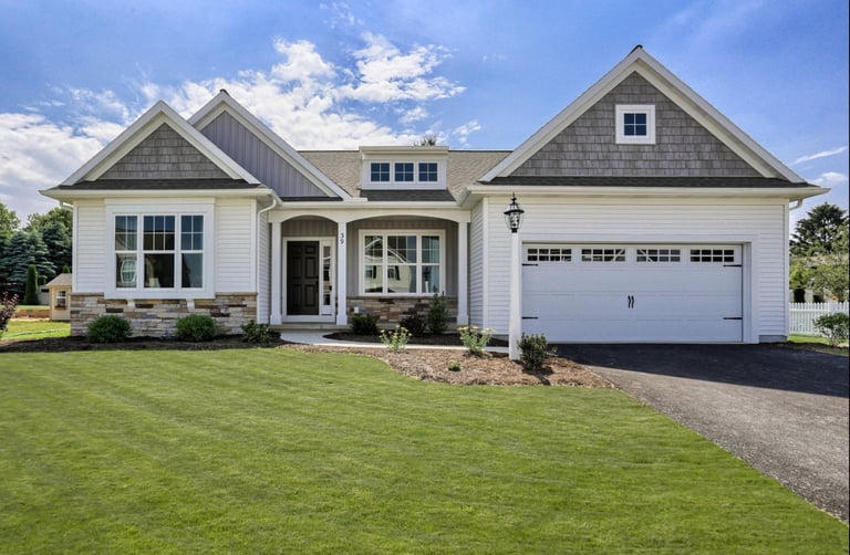 Modern white ranch house with stone accents, a green lawn, and a two-car garage under a blue sky.