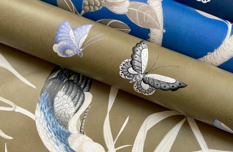 Rolls of luxury designer wallpaper featuring bird and butterfly motifs in blue and gold colors.