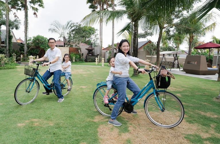 Family biking together during extended family photography session at Lumbini Villas Jimbaran Bali in a tropical garden