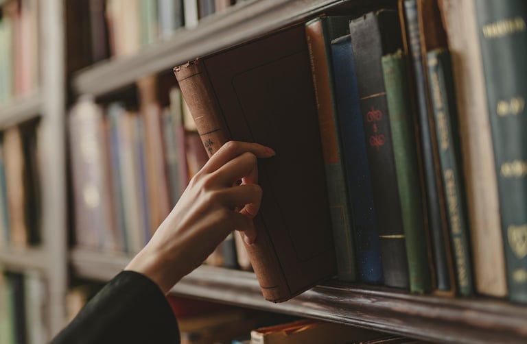 Hand reaching for a vintage book on a library shelf lined with books