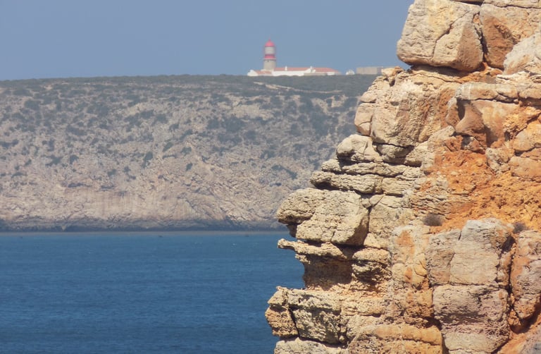 roccia in primo piano con sfondo di oceano e faro che si scorge in lontananza.