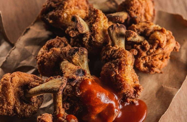 Alitas y muslitos de pollo fritos crujientes, cubiertos con una capa dorada y bañados con salsa