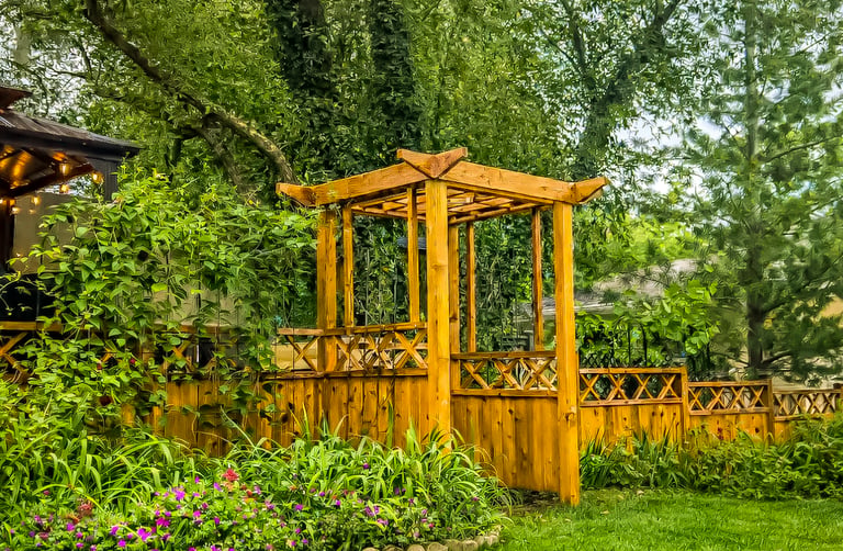 Wooden garden pergola and lattice fence surrounded by lush green plants and colorful flowers.