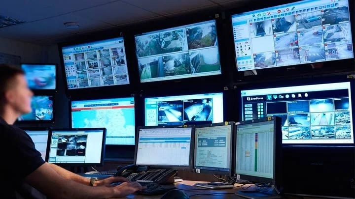 Security operator monitoring a multi-screen CCTV surveillance system in a modern control room.
