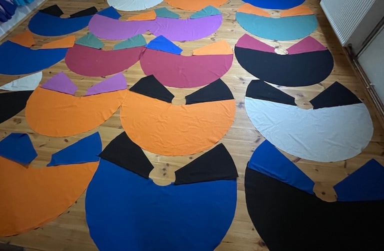 Handmade colorful circle capes in various vibrant fabrics laid out on a wooden floor for sewing.