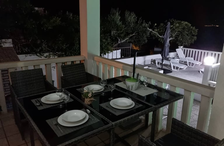 The photograph shows the apartment balcony with a dining set at night.