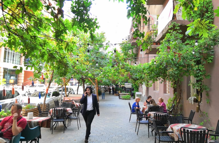 a woman walking down a sidewalk with people sitting at tables