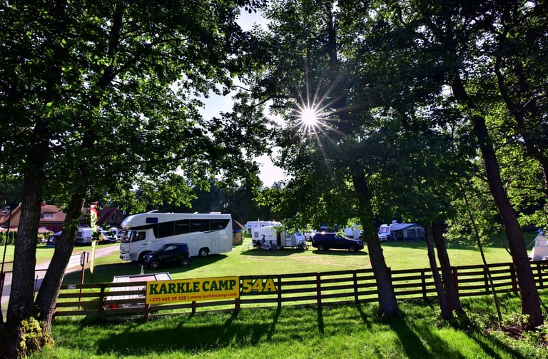 Sunny RV park at Karkle Camp with motorhomes and caravans parked on green grass under shady trees.
