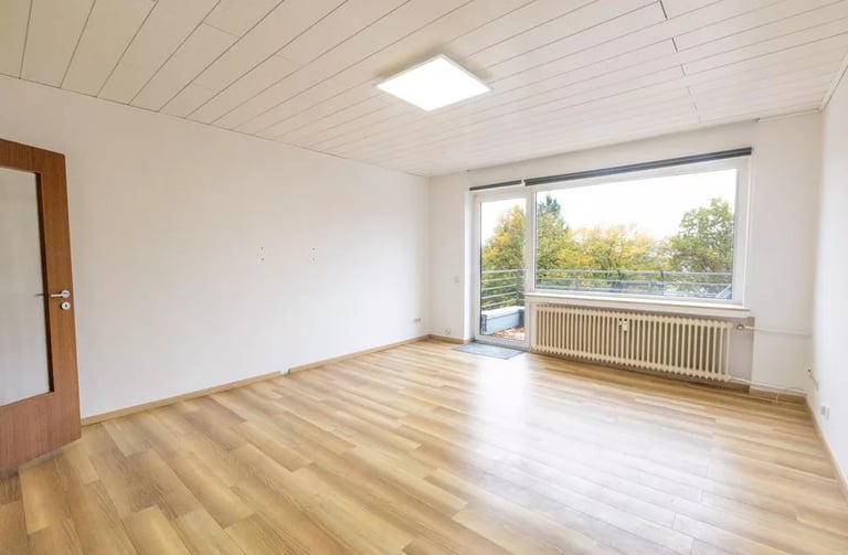 Leeres, modernes Wohnzimmer mit hellem Laminatboden und einem großen Fenster mit Blick auf einen Balkon.