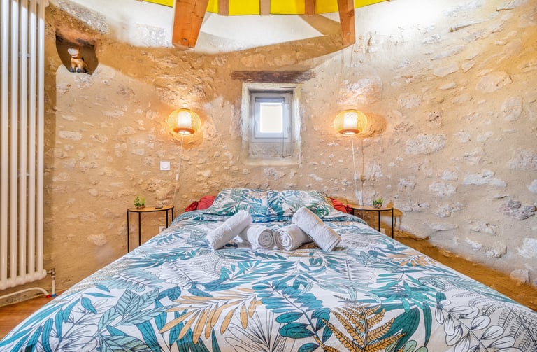 Chambre d’hôte dans un moulin rénové – lit double, serviettes pliées, murs en pierre et lumière natu