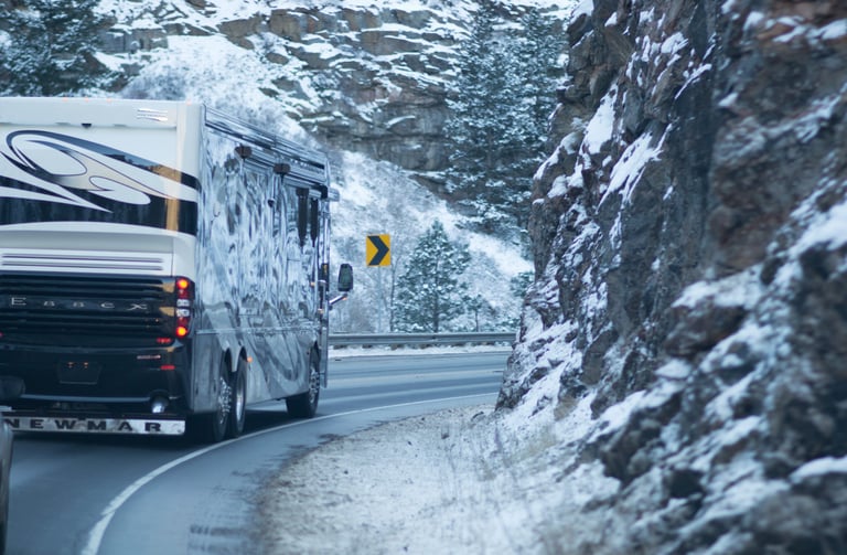 A luxury Newmar Essex motorhome driving along a winding mountain highway in winter snow.