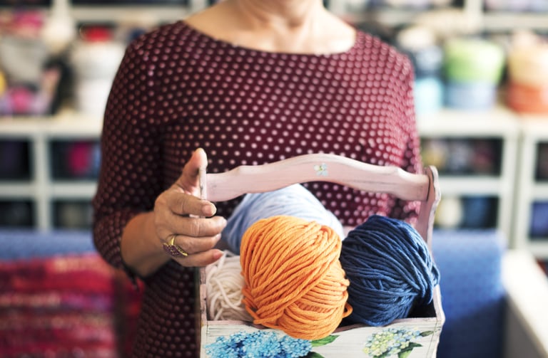 una mujer con un conetedor de madera con varios estambres