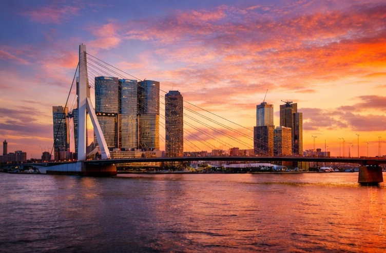 Rotterdam skyline and Erasmus Bridge at sunset with vibrant orange clouds over the Maas river.