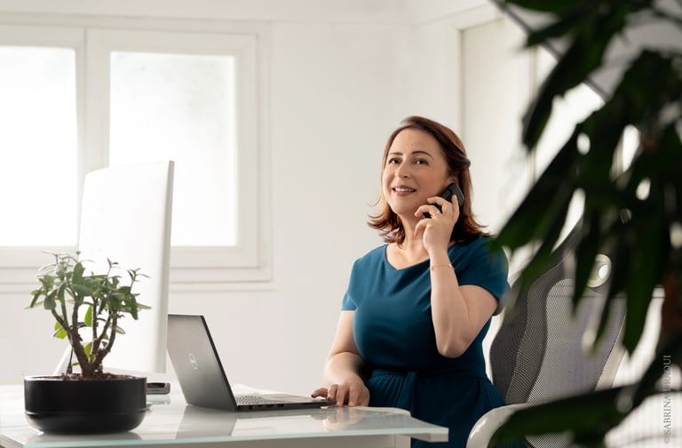 a corporate woman sitting at a desk with a laptop and talking on the phone