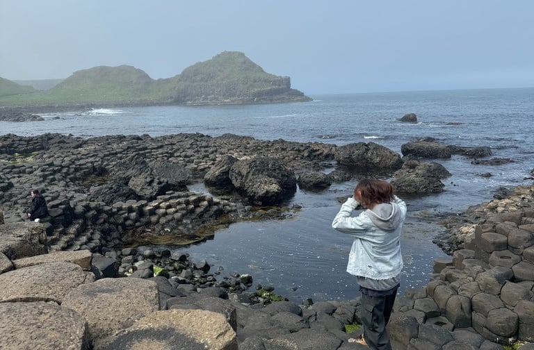 a person standing on a rock formation in the ocean, Ireland, Giant Causeway