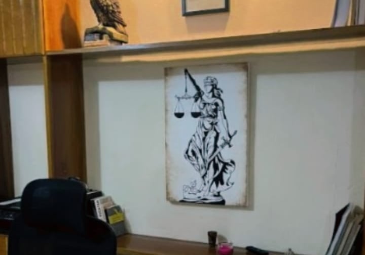 Pared blanca de oficina con repisas. Un diploma, un cuadro decorativo alusivo a la justicia y un buho