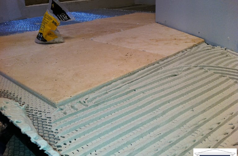 Close-up of hands laying beautiful natural stone tiles on a floor in a cozy bathroom in Palatine IL.