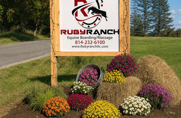 Wooden Ruby Ranch sign for equine boarding and horse massage, featuring fall mums and hay bales.