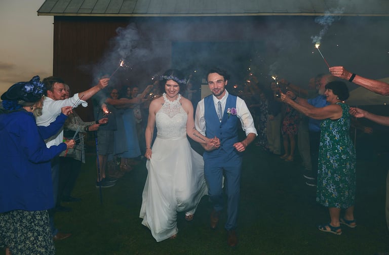a bride and groom walking through guests sparklers path at a wedding party