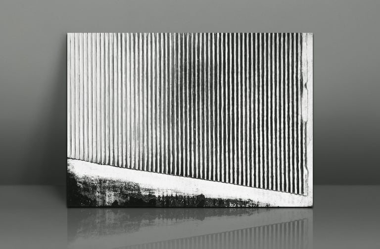 Black and white abstract art print with vertical corrugated lines leaning against a grey wall.