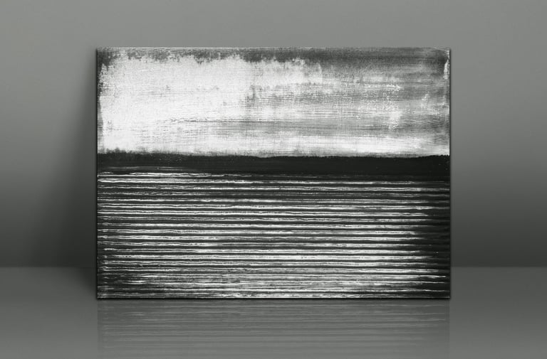 Black and white abstract landscape painting of a lake shore on canvas leaning against a wall.