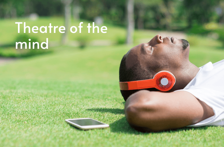 Person lying on grass with eyes closed listening to audio books sound design through headphones