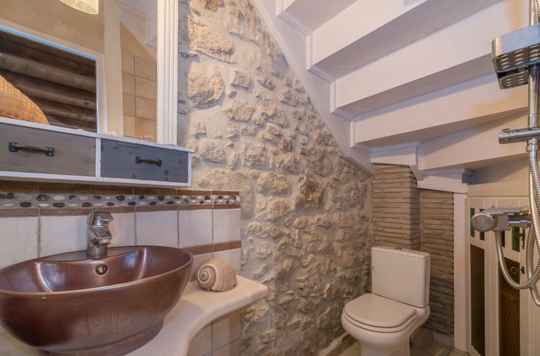Bathroom under wooden stairs with stone wall in Villa Galanoussa