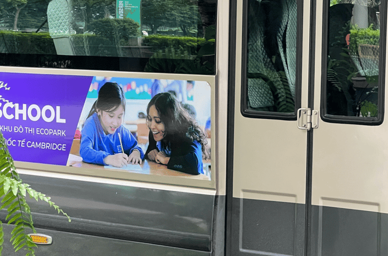 A bus with a advertisement of a school. The advertisement has a female teacher teaching students.
