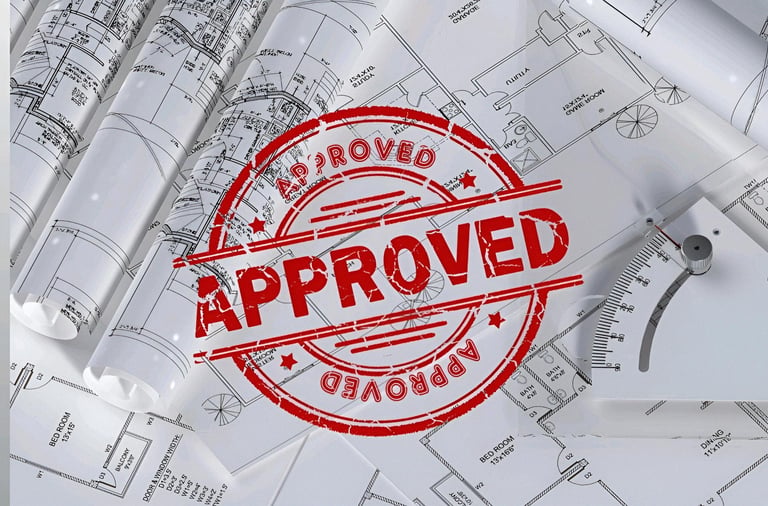Red approved rubber stamp on architectural blueprints for a home construction project.
