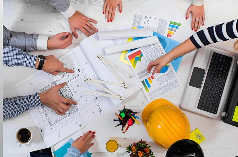 Professional engineering team reviewing architectural blueprints and project data on a white office desk.
