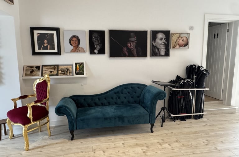 Photography studio interior with a teal velvet chaise longue and wall-mounted portrait gallery.