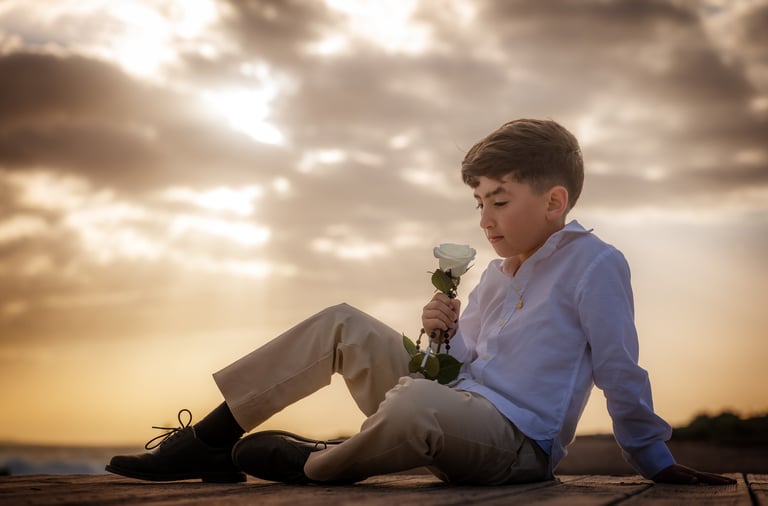 a boy sitting on a wooden deck with a flower