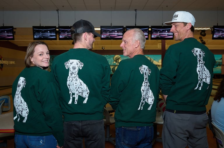 Four smiling people at a bowling alley wearing matching green sweatshirts with Dalmatian dog graphics.