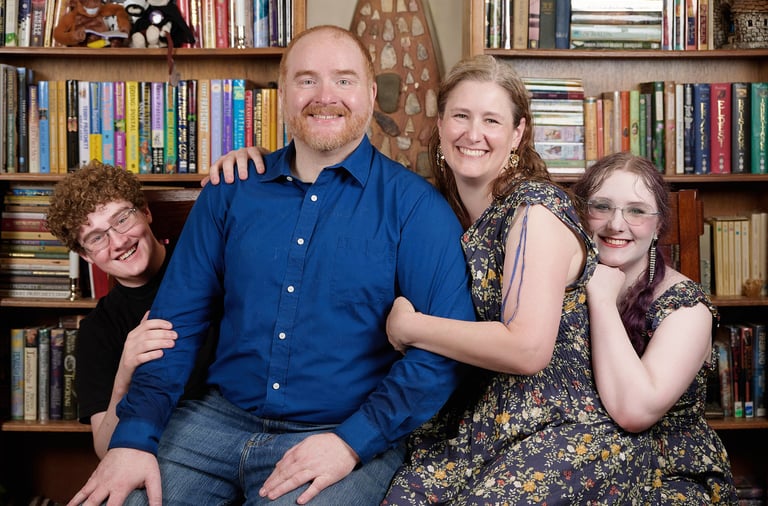 a man and woman sitting on a couch with their kids on both sides in front of a bookshelf