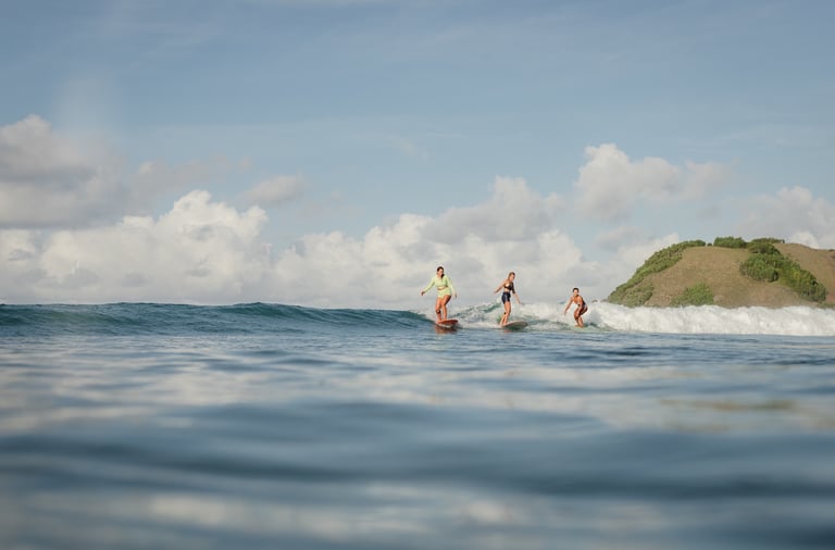 Three surf students riding the same wave on longboards, smiling and having fun.