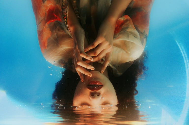 Retrato artístico invertido de uma mulher submersa em água azul clara com reflexos e bolhas.