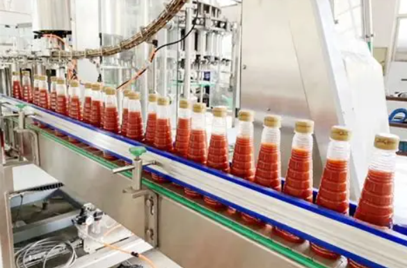 Glass bottles of red sauce moving along an automated conveyor belt in a food production factory.