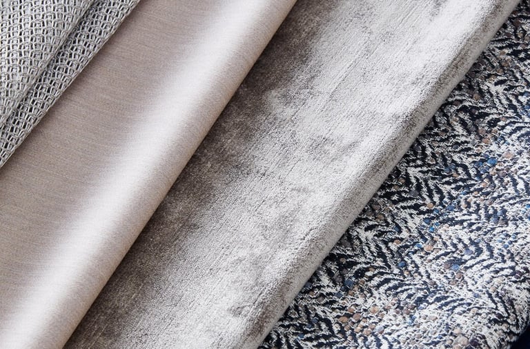 A collection of luxury upholstery fabric swatches in neutral grey, beige, velvet, and patterned textures.