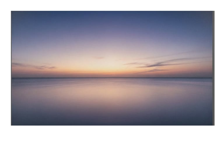 A serene ocean horizon at sunset with soft purple and orange hues over calm water.