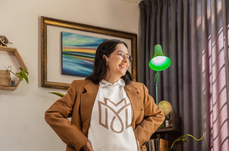 Femme souriante en veste marron et un sweat-shirt arborant un logo monogramme debout dans un bureau.