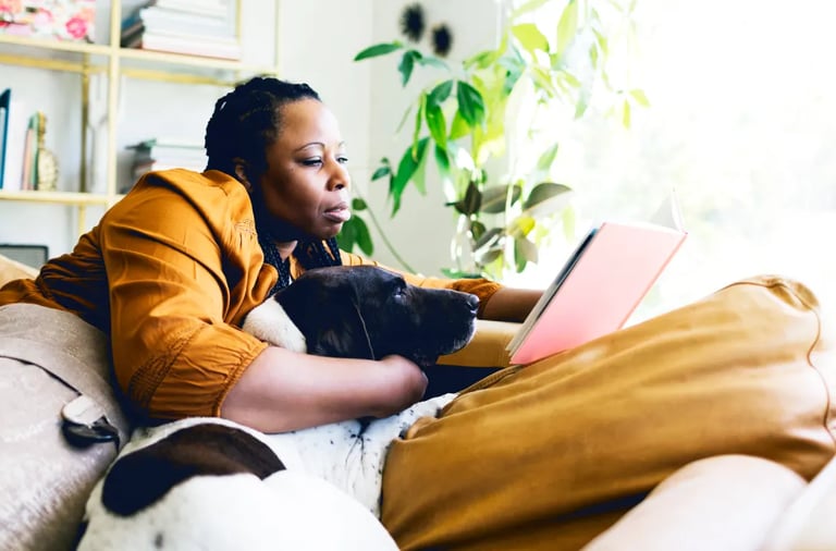 Una mujer afro sentada en un sofá con un perro y leyendo